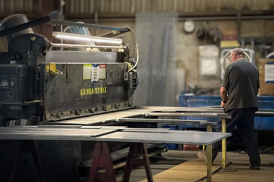 worker pushing plate into shear